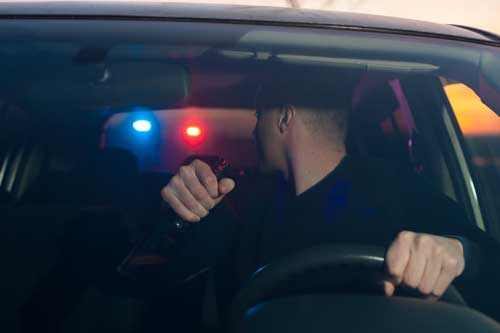 A man being pulled over by the police while holding a beer bottle. 