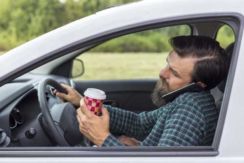 A distracted driver talking on the phone and holding a coffee. 