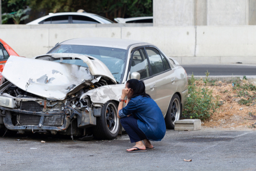 A woman squatting down beside her car after an accident.