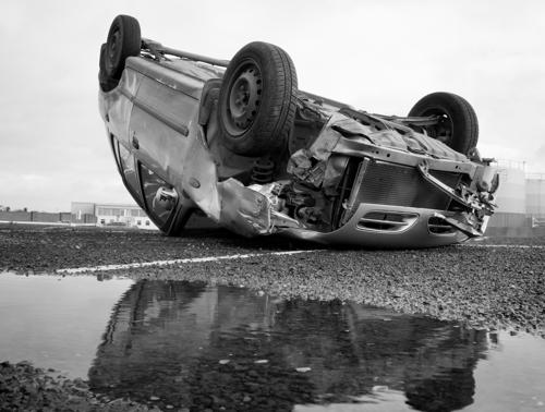 A car lying upside down on a wet road.